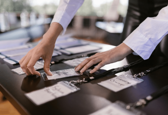 De nombreux badges de participants à un événement professionnel posés sur une table noire et manipulés par une organisatrice. Photo utilisées dans un article sur les rendez-vous IA.