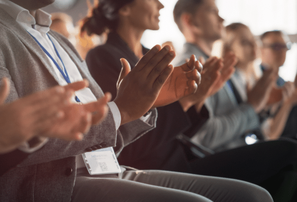 Plusieurs personnes assistant à une conférence en train d'applaudir. Illustre l'article sur les salons IA de l'été 2025.