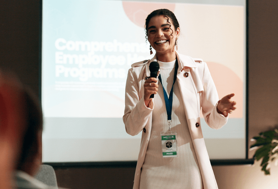 Femme d’affaires, séminaire et formation pour intervenant dans la salle de conférence pour présentation bien-être. Éducation, discours de forum et micro avec coach d’entreprise sur scène pour les relations publiques ou le développement. Image utilisée pour l'article LabSense sur les événements IA de l'hiver 2025/2026.
